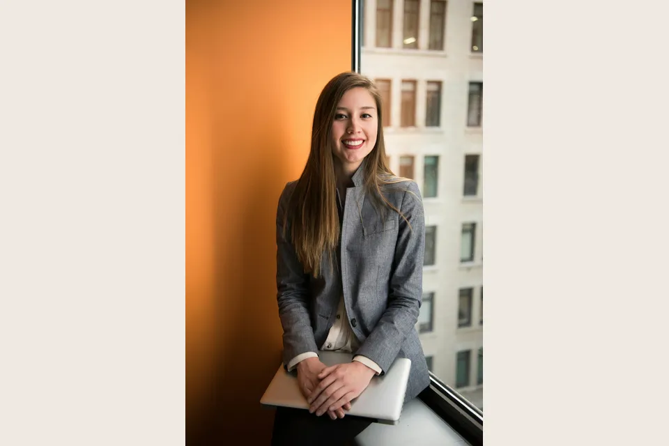 A professional holding a laptop beside a bright office window